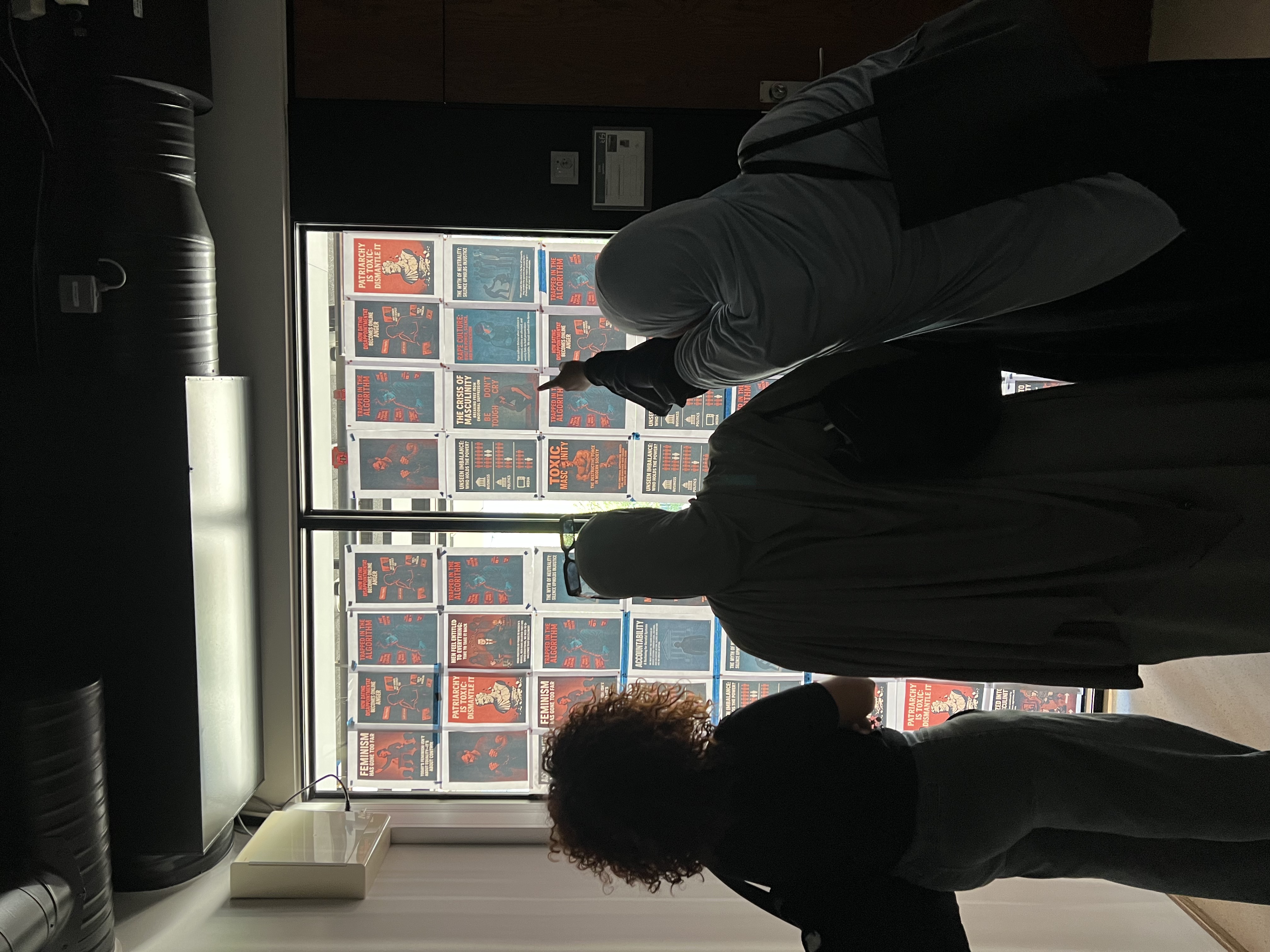 Tre deltakere som observerer plakatveggen med rødt lys. De ser fokusert og alvorlig ut.